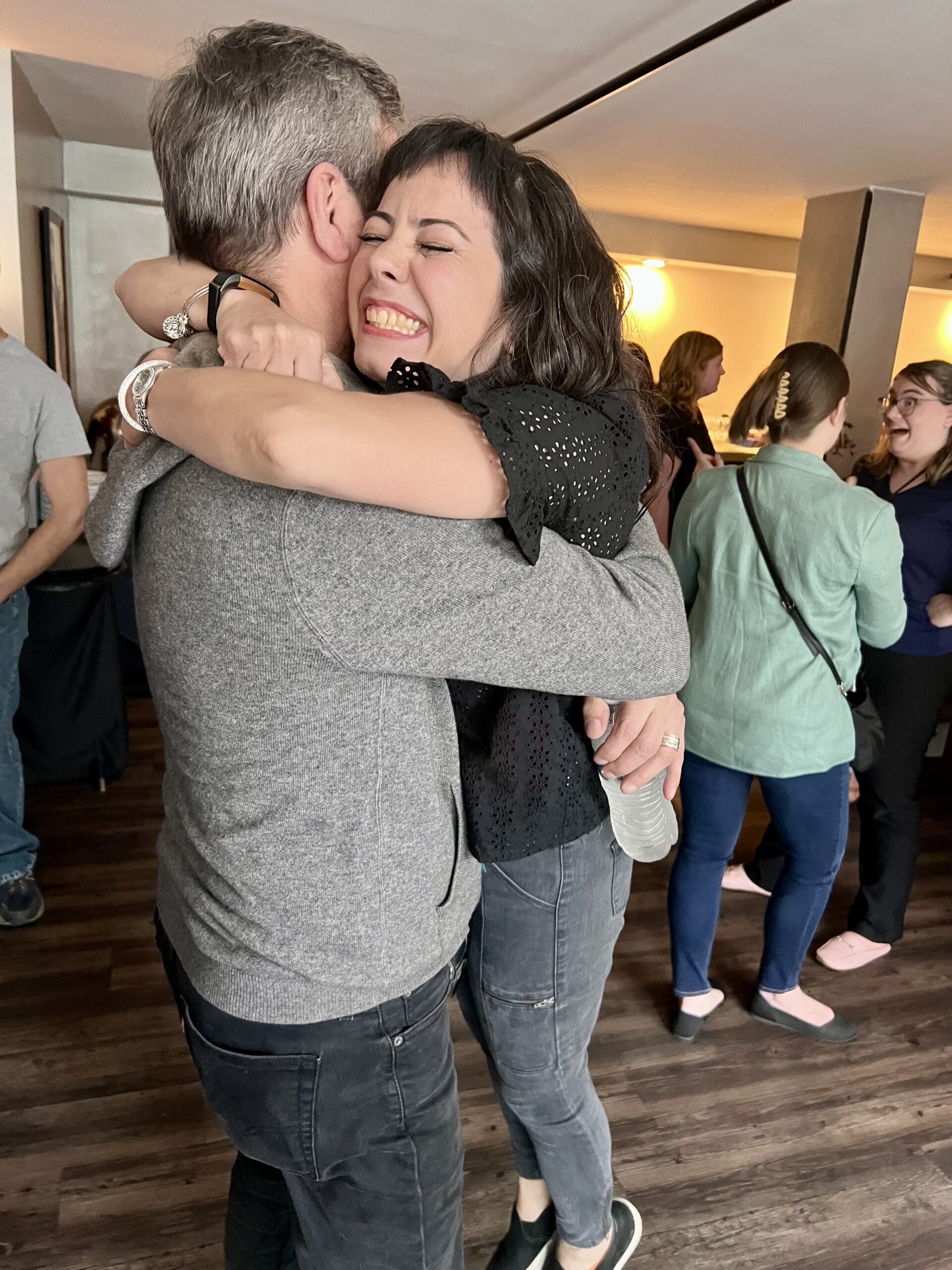 two people hug in the foreground, with others mingling behind them